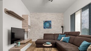 Un salon moderne avec un canapé d’angle, un téléviseur à écran plat, une table basse et une étagère fixée au mur.