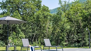 Une piscine avec deux chaises longues et un parasol, entourée d’une végétation luxuriante et avec une chaîne de montagnes en toile de fond.
