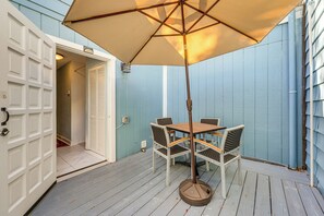 Eine Terrasse mit Tisch und Stühlen unter einem Sonnenschirm, eine weiße Garagentür und eine blaue Außenwand.