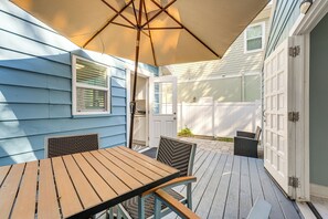 Eine Holzterrasse mit Tisch und Stühlen, eine weiße Tür und ein beiger Sonnenschirm.
