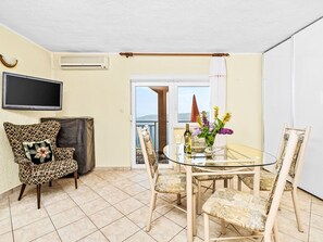 A living room with a TV, patterned armchairs, a glass table with chairs, and a view of the sea through a balcony door. - Panoramare by Interhome (Plomin)