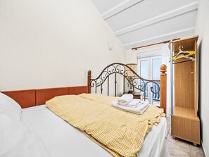 A bedroom with a bed, a wooden wardrobe, a window with a view, and a ceiling with exposed beams. - Panoramare by Interhome (Plomin)