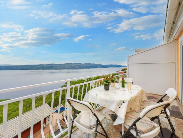 Un balcón con mesa y sillas, con vista a un lago y montañas distantes.