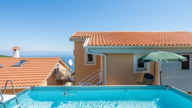 A swimming pool with a clear view of the sea in the background, a tiled roof, and a small window with a chair and umbrella. - Panoramare by Interhome (Plomin)