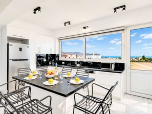 A modern kitchen with a dining area, large windows, and a view of the sea. - Luminosa Luxus-Villa by Interhome (Georgioupoli)