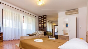 Hotellihuone, jossa on sänky, tuoli, pieni pöytä, vaatekaappi ja kylpyhuone, joka näkyy avoimesta ovesta.