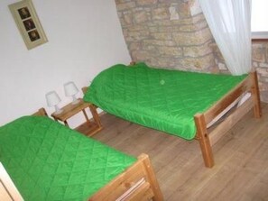 Zwei hölzerne Betten mit grüner Bettwäsche in einem Zimmer mit Steinwänden und einem weißen Vorhang.