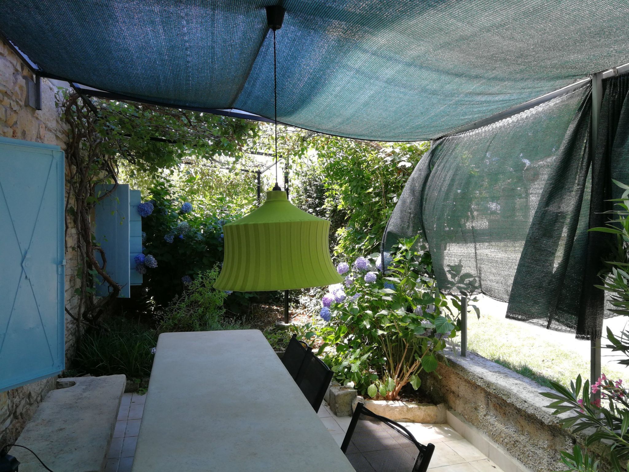 A patio with a table and chairs, surrounded by greenery and a hanging light fixture.