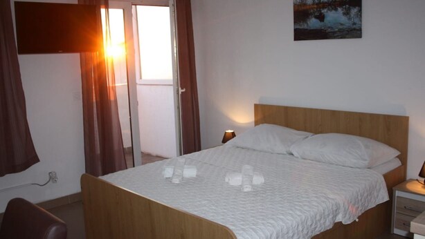 A bedroom with a wooden bed, white bedding, a nightstand, a lamp, and a painting on the wall. - Studio-Apartment mit Balkon by Interhome (Omiš)