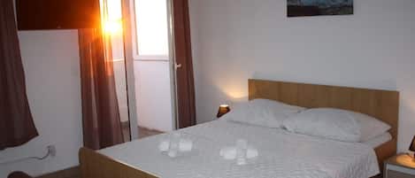 A bedroom with a wooden bed, white bedding, a nightstand, a lamp, and a painting on the wall.