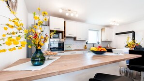 A modern kitchen with white cabinets, a wooden countertop, and a central island with a bowl of fruit.