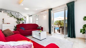 A modern living room with a red sofa, a white coffee table, and a view of a pool through a glass door.