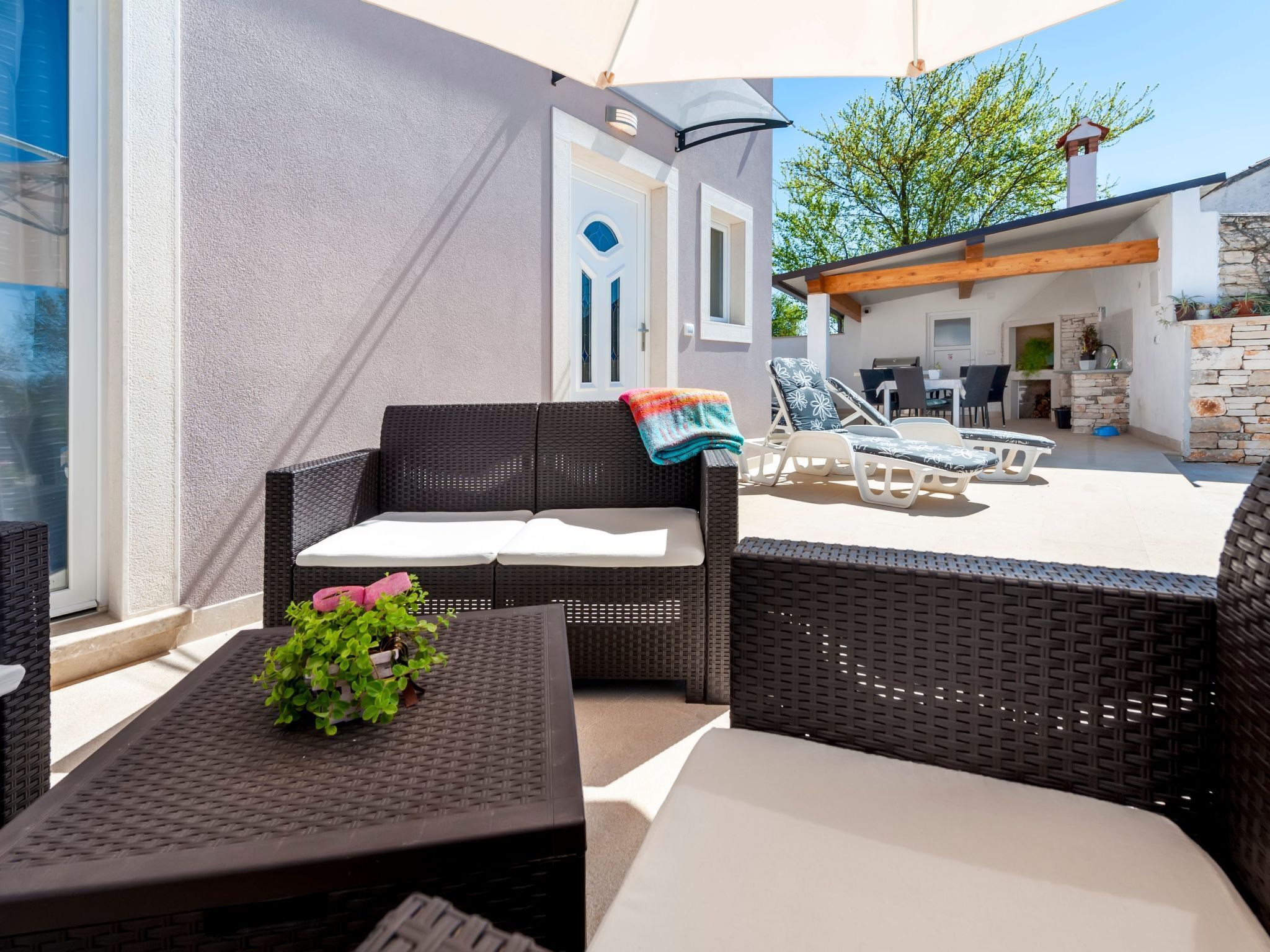 Un espace patio extérieur aménagé avec des meubles en osier, un canapé blanc et une table agrémentée d’une plante.