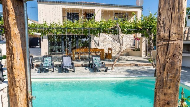 Ein Poolbereich mit einer Holzpergola, Liegestühlen und einem Gebäude im Hintergrund.