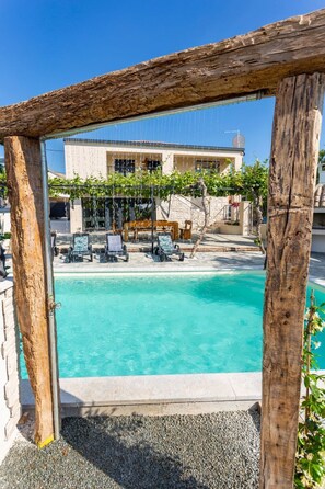 A pool area with a wooden pergola, lounge chairs, and a building in the background. - Schönes Ferienhaus in Modrusani mit Großem Garte by Interhome (Cere)