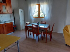 Eine kompakte Küche mit Kühlschrank, Holzschränken, einem Esstisch mit Stühlen und einem gelben Sofa.