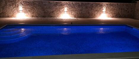 A swimming pool with blue tiles and a stone wall with lights.