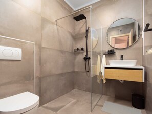A modern bathroom with a glass-enclosed shower, a white sink, and a round mirror. - Designer Villa Simone - Modern und Heritage Style by Interhome (Jakovici)