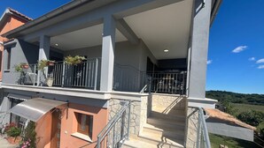 Un bâtiment à deux étages doté d’un balcon couvert, d’un escalier en pierre et offrant une vue sur la campagne.