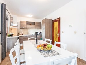 A modern kitchen with a dining area, white furniture, and a fruit bowl on the table.