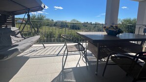 Un balcon avec une table et des chaises, un espace salon abrité et une vue sur un paysage verdoyant.