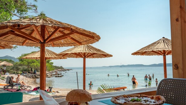 A beachside restaurant with outdoor seating, umbrellas, and a view of the sea. - Mobilheim direkt am Strand by Interhome (Ugljan/Ugljan)
