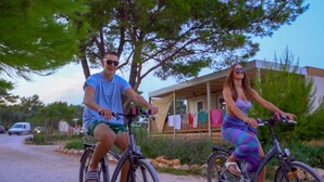 Two people riding bicycles on a gravel path with a building in the background. - Mobilheim direkt am Strand by Interhome (Ugljan/Ugljan)