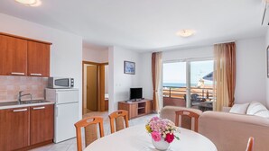 Um apartamento moderno com cozinha, sala de jantar e sala de estar. Possui uma varanda com vista para o mar.