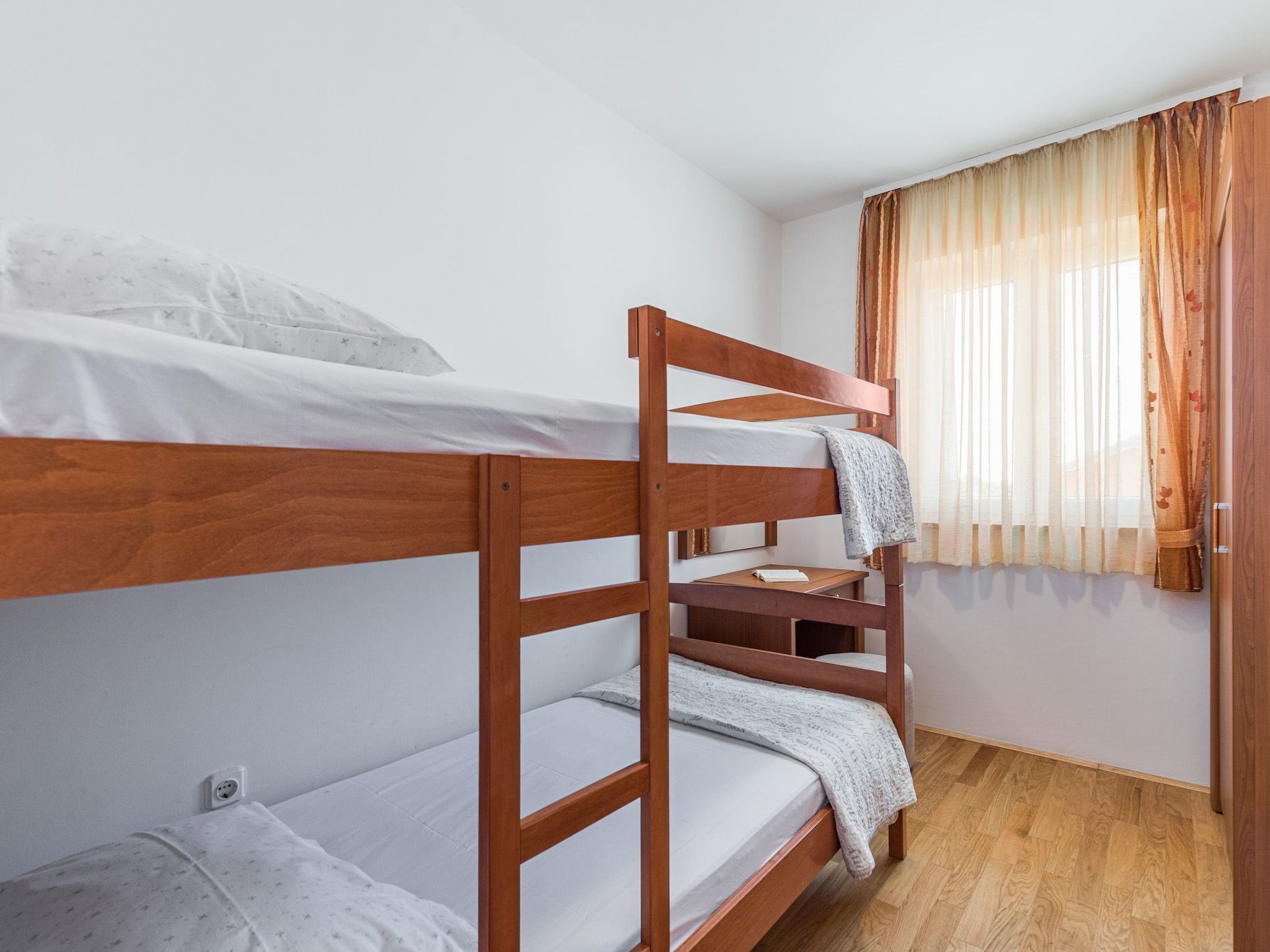 Une chambre avec un lit superposé, une structure en bois, du linge de lit blanc et une fenêtre ornée de rideaux légers.