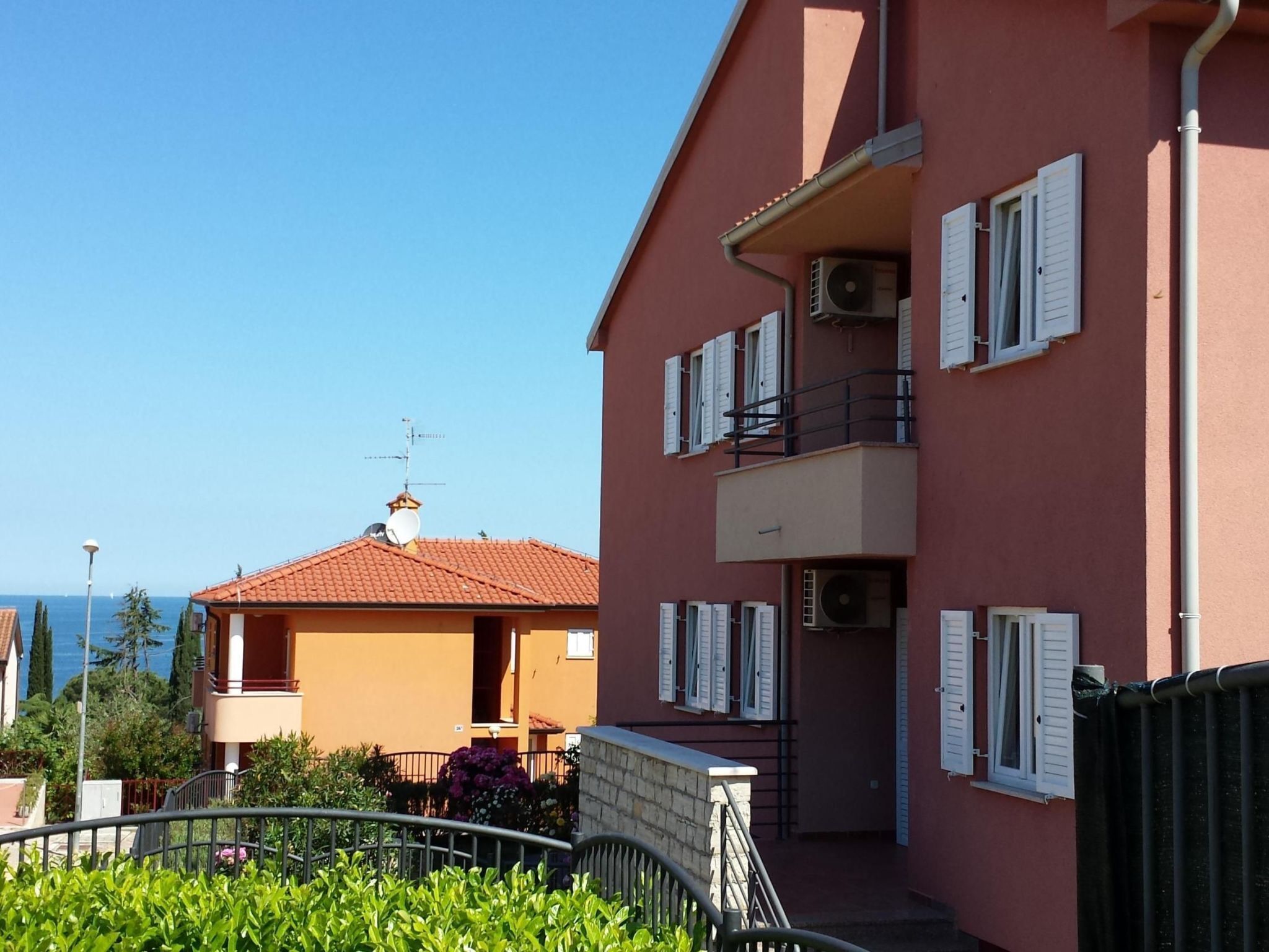 A multi-story building with balconies, a red-tiled roof, and a clear view of the sea.