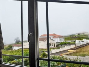 Une vue à travers la fenêtre d’un bâtiment dont le toit est rouge, entouré de verdure et d’autres constructions.