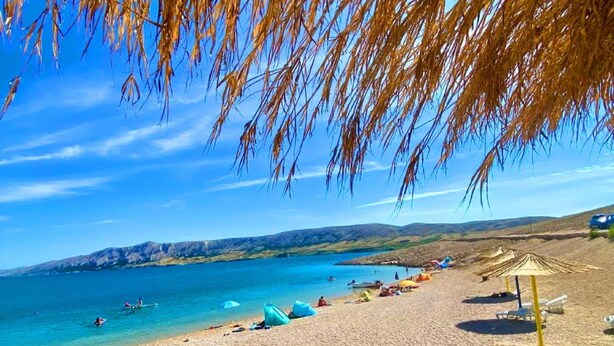 Een strand met helderblauw water, mensen die zwemmen en parasols.