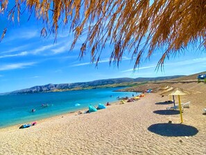 Une plage avec une eau d’un bleu limpide, des gens qui se baignent et des parasols.