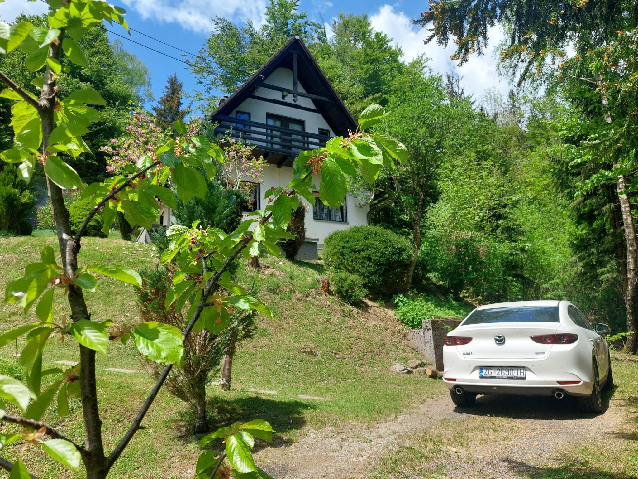 Une voiture blanche est garée devant une maison dont le toit est en pente et dont on peut voir la porte du garage.