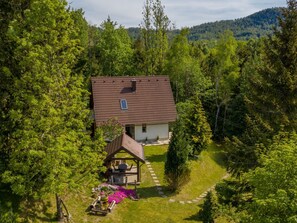 A house with a tiled roof, surrounded by dense forest, and a small outdoor seating area with a table and chairs. - direkt am Strand by Interhome (Delnice)