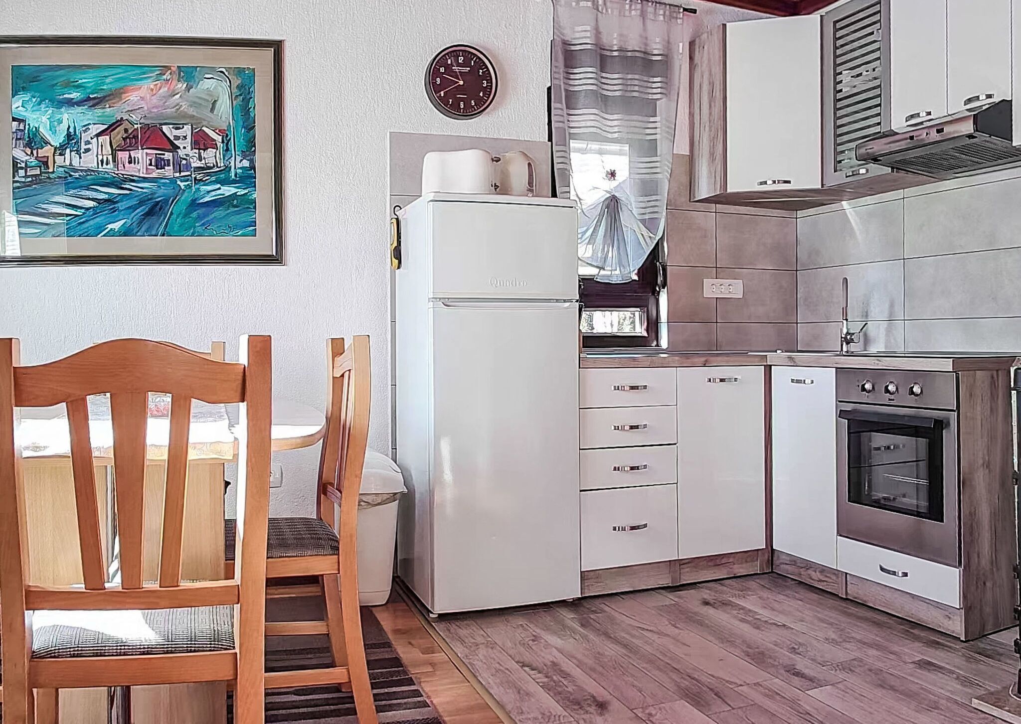 Une cuisine de taille réduite, équipée d’un réfrigérateur, d’une cuisinière et d’une table à manger en bois avec des chaises.