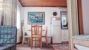 Een ruime kamer met een eettafel, stoelen, een bank, een bed, een koelkast, een klok en een schilderij aan de muur.