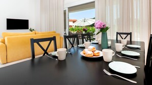 Ein modernes Wohnzimmer mit einem gelben Sofa, einem Esstisch gedeckt mit Tellern, Tassen und einem Blumenstrauß.