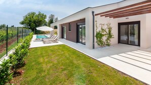 Ein modernes Haus mit Swimmingpool, überdachter Terrasse und gepflegtem Rasen.