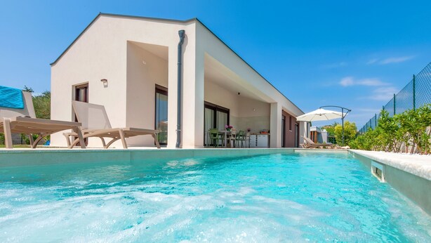 Ein moderner Poolbereich mit Liegestühlen, einem Pool und einem Gebäude mit großen Fenstern und Türen.