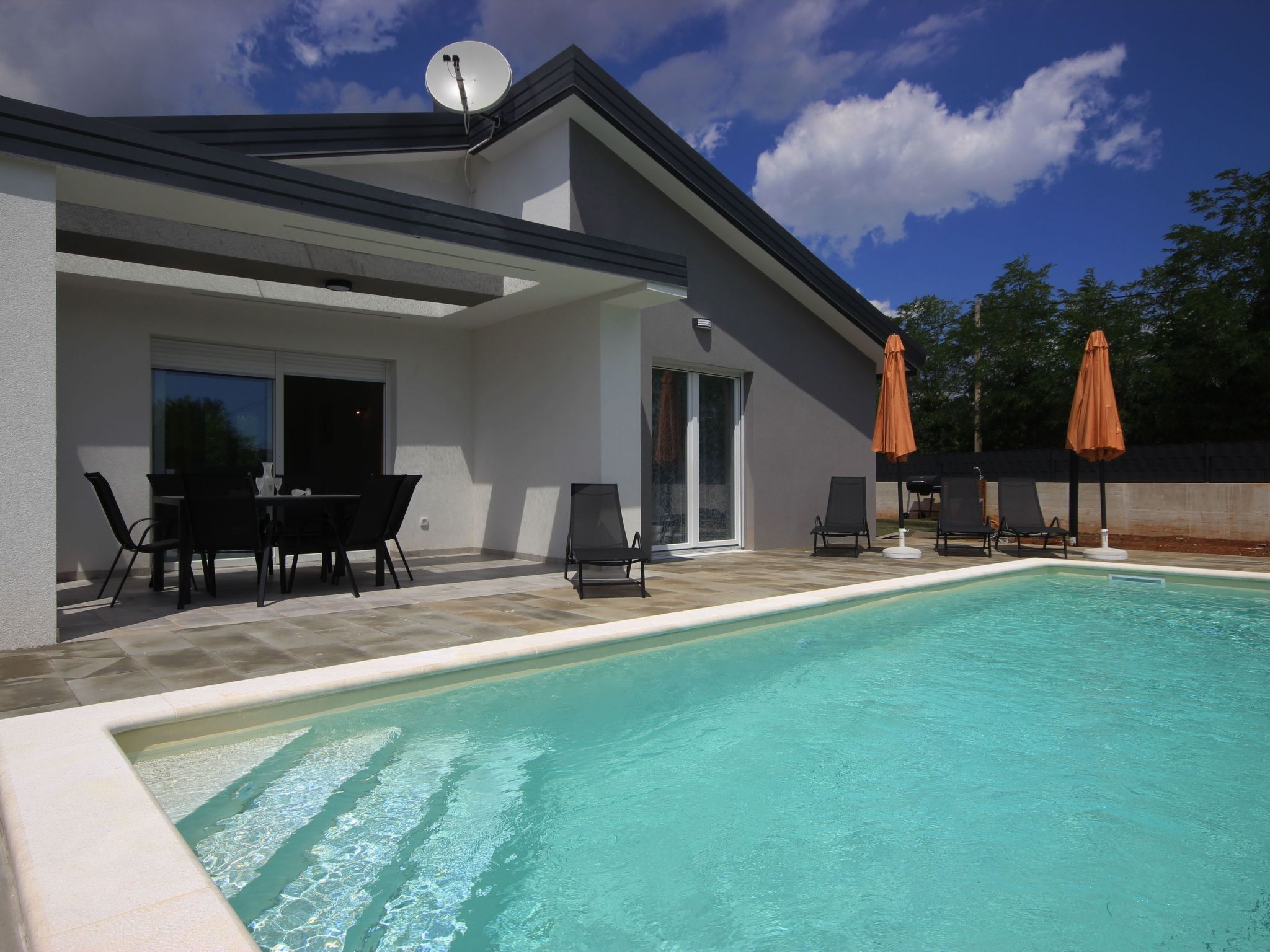 Una casa moderna con piscina, mobiliario exterior y antena parabólica.