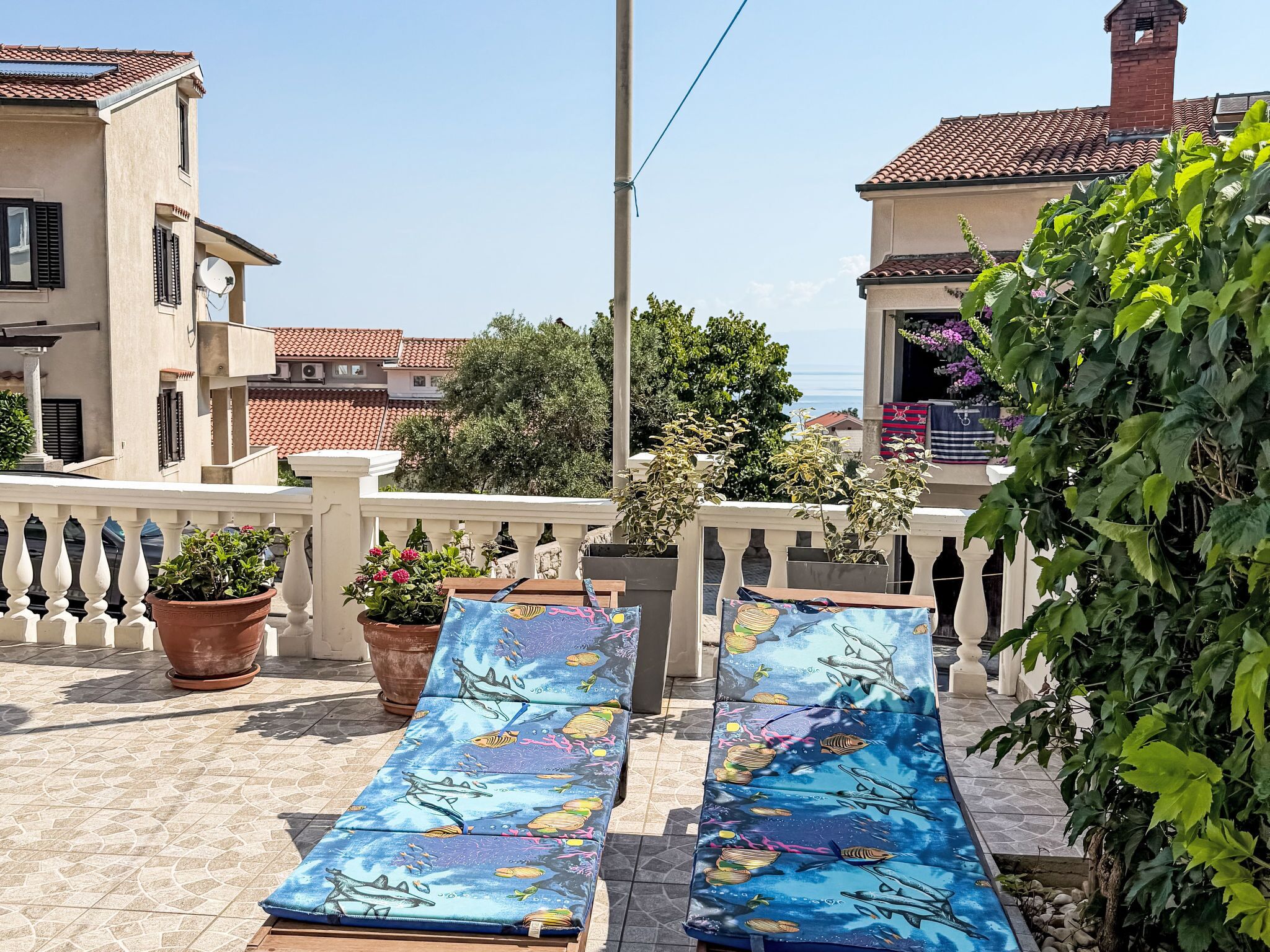 A terrace with two lounge chairs, potted plants, and a view of the sea and buildings.