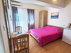A bedroom with a bed, a desk, a chair, a wardrobe, and a painting on the wall.