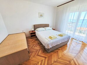 Un dormitori amb un llit, taules de nit, una làmpada, un quadre a la paret i una vista per la finestra.