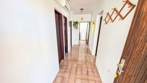 Um corredor com piso de azulejos, paredes brancas e portas de madeira.