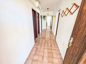 Un passadís amb paviment de rajoles, parets blanques i portes de fusta.