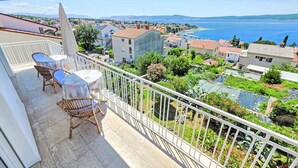 Varanda com cadeiras de vime e uma mesa, com vista para uma vila costeira com edifícios e um porto de recreio.