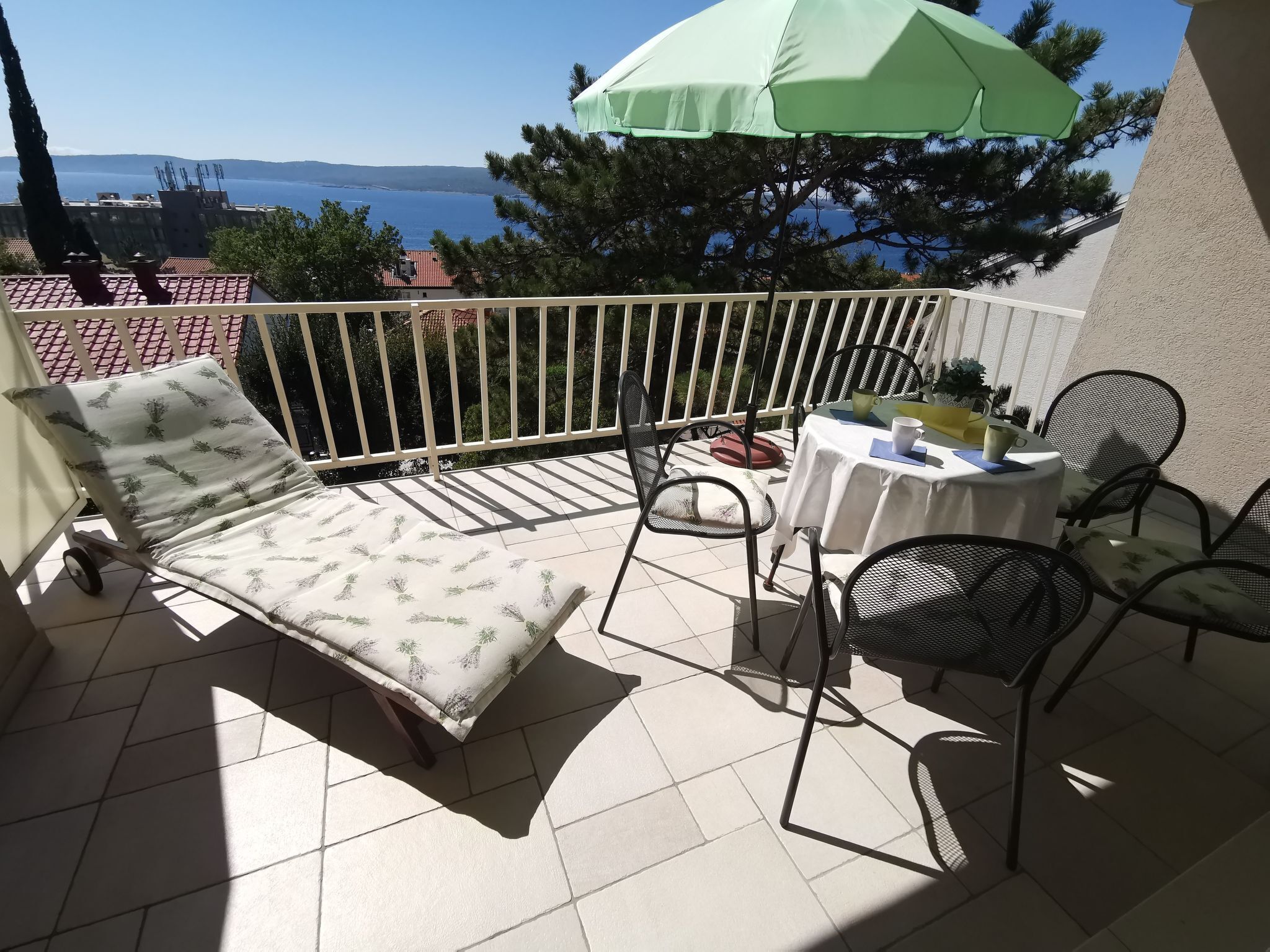 Een balkon met een lounge stoel, een tafel met stoelen en een groene parasol.