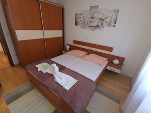 Ein ordentlich bezogenes Bett mit rosa und weißen Textilien, einem hölzernen Kopfteil und einem an der Wand befestigten Blumenbild.