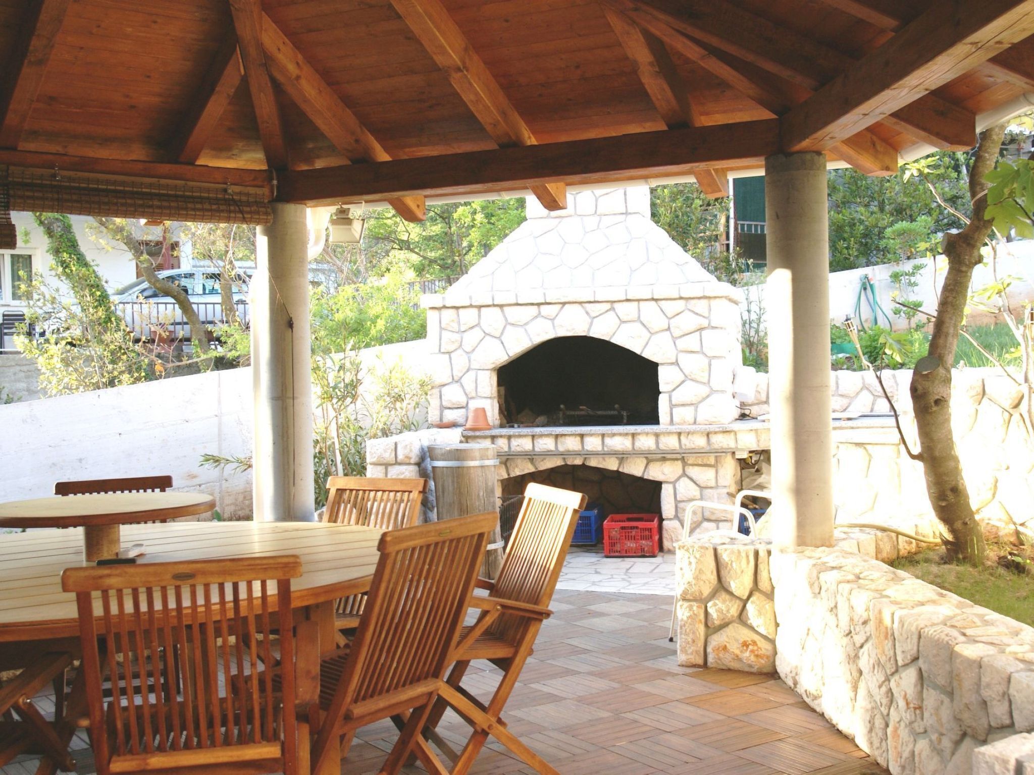 Une terrasse extérieure dotée d’un four à pizza en pierre, de meubles en bois et offrant une vue sur un quartier résidentiel.